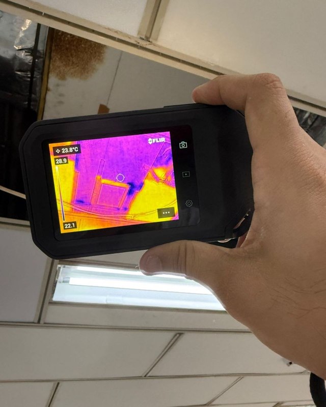 Câmera termográfica FLIR apontada para um forro com mancha de infiltração, durante inspeção técnica.